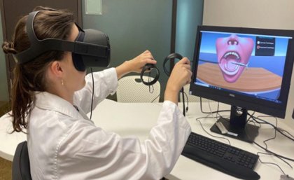 UQ School of Dentistry students use virtual and augmented reality technologies to hone their skills. a person in white coat wears virtual reality glasses and holds handsets in front of a screen with an image of a mouth and teeth